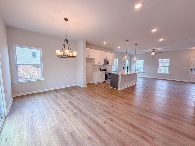 kitchen with stainless steel appliances, a kitchen island with sink, sink, white cabinetry, and hanging light fixtures