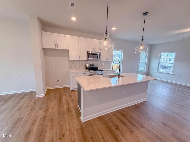 kitchen with appliances with stainless steel finishes, sink, decorative light fixtures, white cabinets, and an island with sink