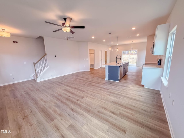 interior space with ceiling fan, a kitchen island with sink, sink, decorative light fixtures, and white cabinets