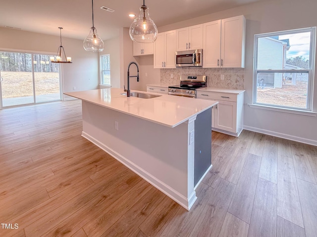 kitchen featuring stainless steel appliances, a kitchen island with sink, sink, decorative light fixtures, and white cabinetry