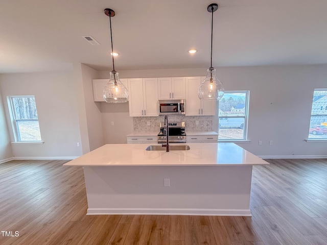 kitchen with sink, an island with sink, decorative light fixtures, and appliances with stainless steel finishes