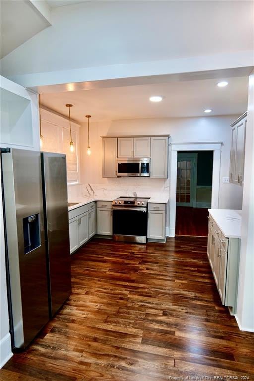 kitchen with hanging light fixtures, vaulted ceiling, appliances with stainless steel finishes, tasteful backsplash, and dark hardwood / wood-style flooring