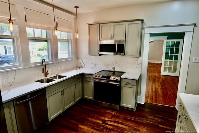 kitchen with sink, dark wood-type flooring, stainless steel appliances, light stone counters, and pendant lighting