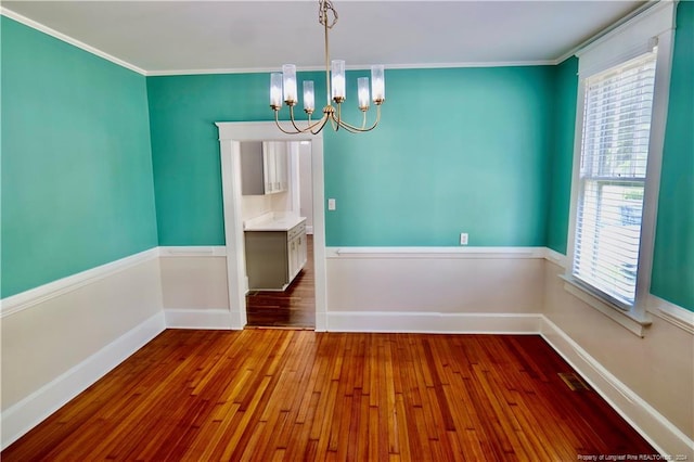 empty room with a chandelier, hardwood / wood-style flooring, and crown molding