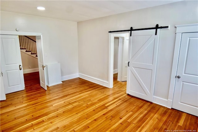 unfurnished bedroom featuring a barn door and light hardwood / wood-style floors