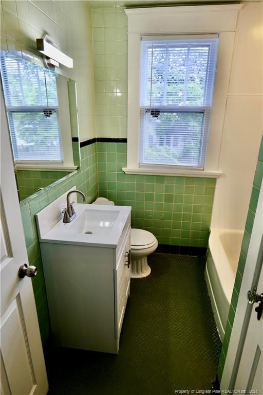 bathroom featuring vanity, a bathtub, toilet, and tile walls