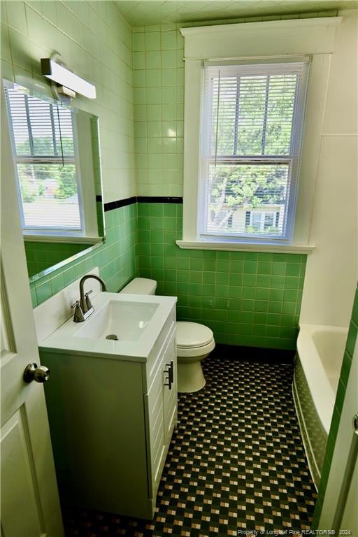 bathroom featuring a washtub, vanity, toilet, and tile walls