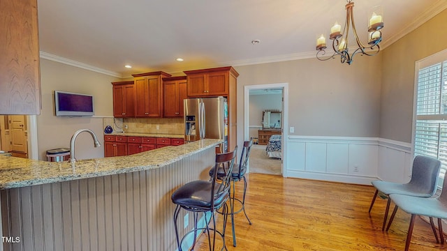 kitchen with a breakfast bar, stainless steel refrigerator with ice dispenser, light stone countertops, a wealth of natural light, and a chandelier