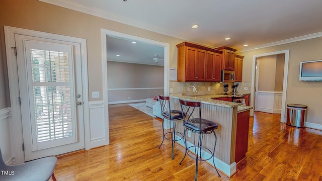 kitchen with light stone countertops, ornamental molding, kitchen peninsula, a kitchen bar, and light wood-type flooring