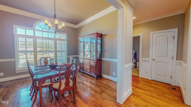 dining room featuring washer / clothes dryer, light hardwood / wood-style flooring, an inviting chandelier, and ornamental molding