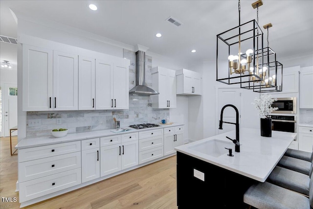 kitchen featuring appliances with stainless steel finishes, backsplash, white cabinetry, and wall chimney range hood