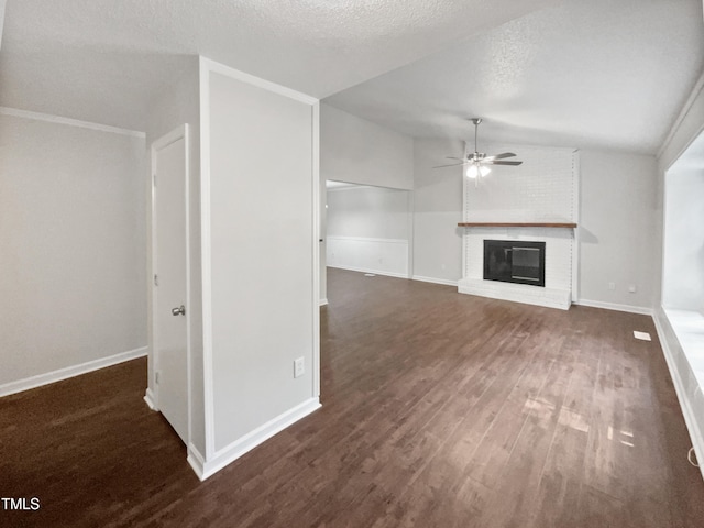 unfurnished living room with brick wall, a fireplace, a textured ceiling, dark wood-type flooring, and ceiling fan