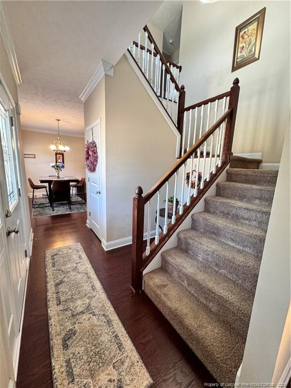 stairs featuring crown molding, hardwood / wood-style flooring, and an inviting chandelier