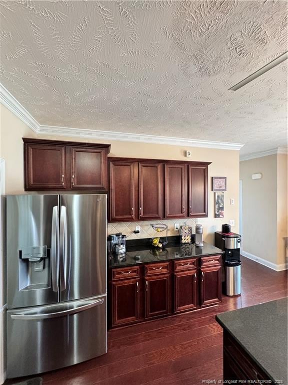 kitchen featuring backsplash, ornamental molding, stainless steel refrigerator with ice dispenser, dark wood-type flooring, and a textured ceiling