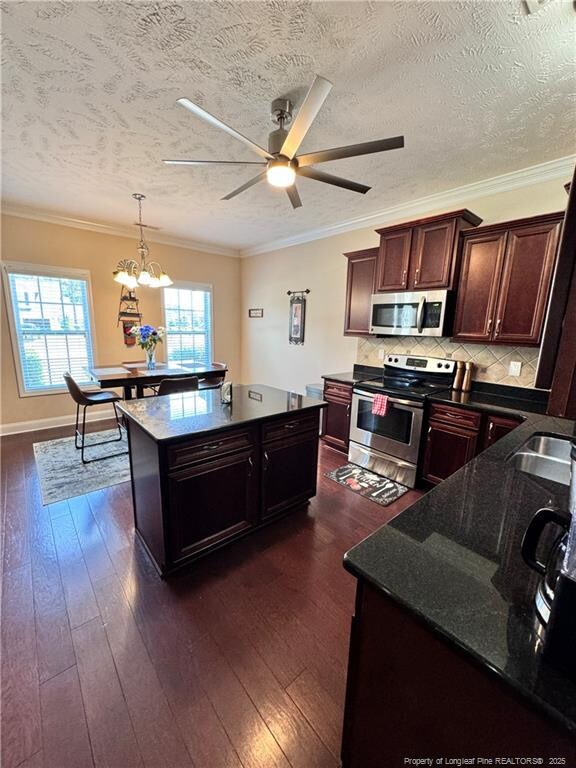 kitchen featuring crown molding, stainless steel appliances, dark hardwood / wood-style floors, a textured ceiling, and decorative light fixtures