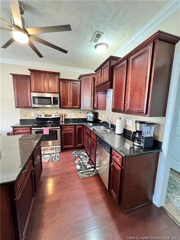 kitchen with appliances with stainless steel finishes, sink, dark stone counters, ornamental molding, and a textured ceiling