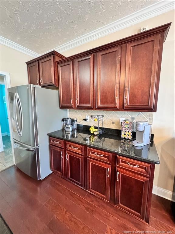 kitchen featuring dark wood-type flooring, crown molding, a textured ceiling, dark stone countertops, and stainless steel fridge