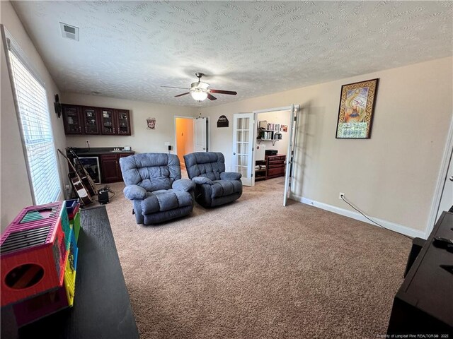 carpeted living room with ceiling fan, french doors, and a textured ceiling