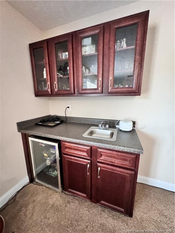 bar with sink, light colored carpet, wine cooler, and a textured ceiling