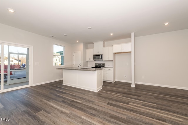 kitchen featuring a kitchen island with sink, white cabinetry, dark stone countertops, stainless steel appliances, and dark hardwood / wood-style flooring