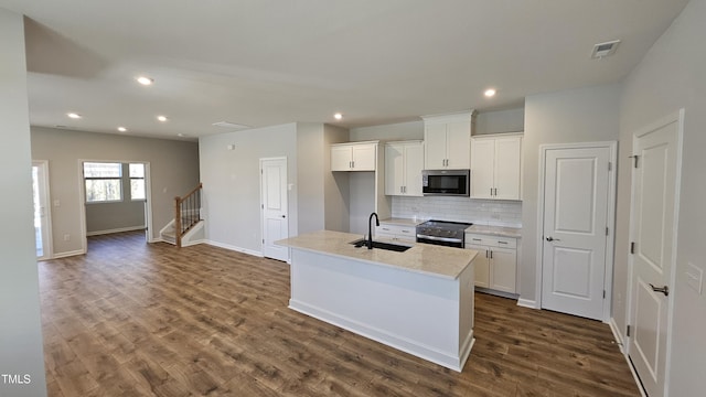 kitchen with white cabinetry, sink, a kitchen island with sink, light stone counters, and stainless steel appliances