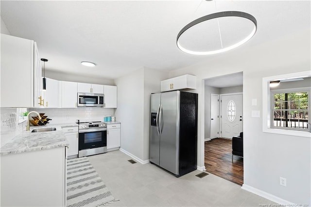 kitchen with white cabinetry, sink, light stone countertops, stainless steel appliances, and backsplash