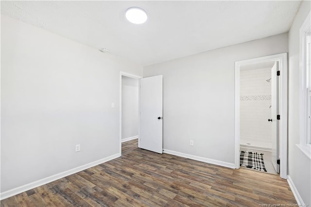 unfurnished bedroom featuring ensuite bathroom and dark hardwood / wood-style flooring