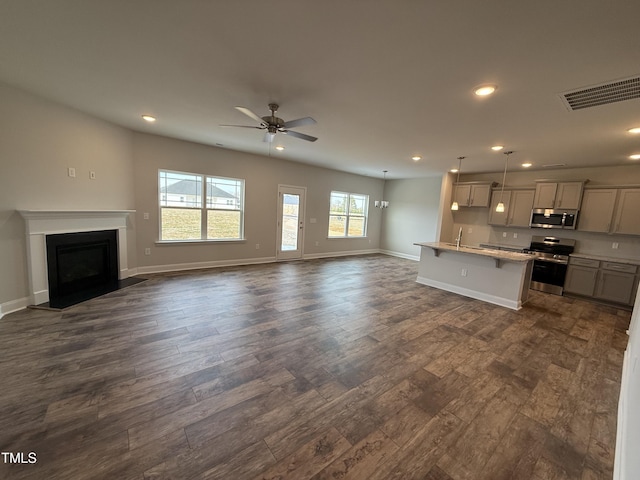 unfurnished living room featuring dark wood-style floors, a fireplace with flush hearth, visible vents, and baseboards