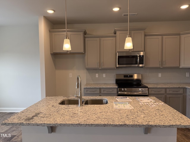 kitchen with decorative light fixtures, a sink, appliances with stainless steel finishes, light stone countertops, and a center island with sink