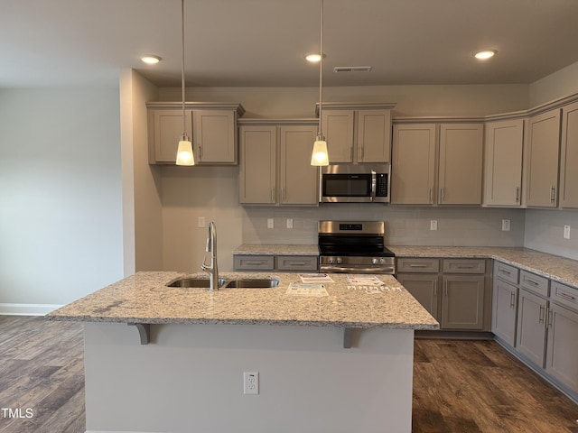 kitchen with stainless steel appliances, hanging light fixtures, a sink, and light stone countertops