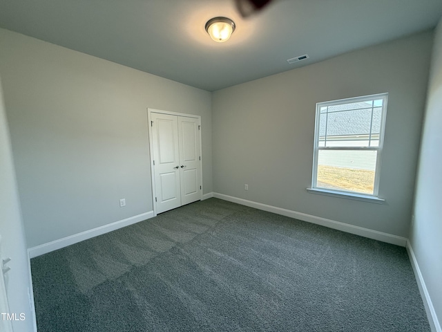 spare room with dark colored carpet, visible vents, and baseboards