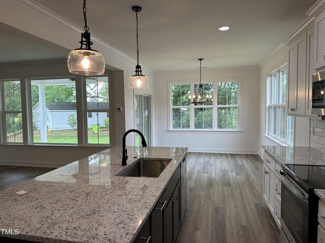 kitchen with sink, a kitchen island with sink, light stone counters, white cabinets, and decorative light fixtures