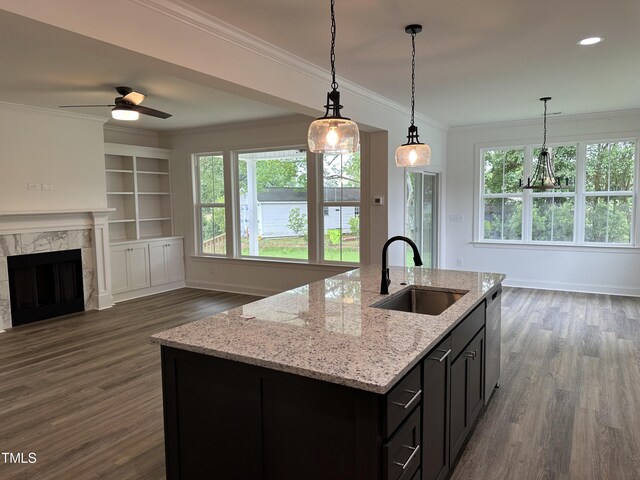 kitchen featuring sink, light stone counters, built in features, pendant lighting, and a kitchen island with sink