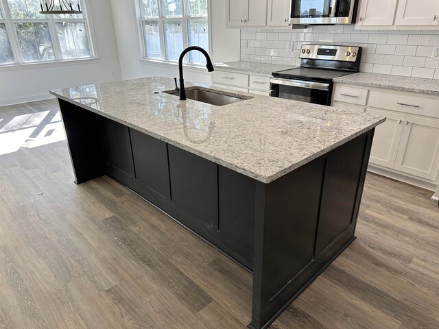 kitchen featuring appliances with stainless steel finishes, an island with sink, sink, light stone countertops, and light wood-type flooring