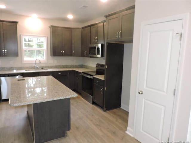 kitchen featuring sink, a kitchen island, light stone countertops, light hardwood / wood-style floors, and stainless steel appliances