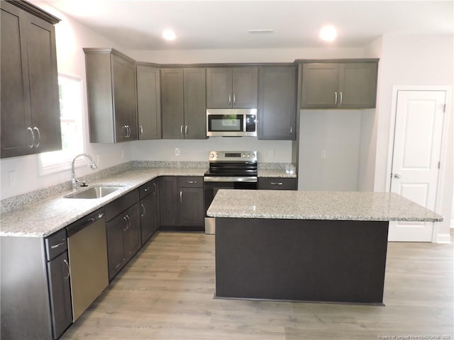 kitchen featuring a kitchen island, light stone counters, sink, and appliances with stainless steel finishes