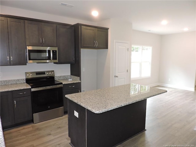 kitchen featuring light wood-type flooring, light stone countertops, a kitchen island, dark brown cabinetry, and stainless steel appliances