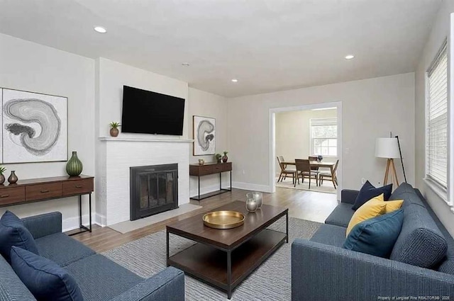 living area featuring a fireplace with flush hearth, baseboards, wood finished floors, and recessed lighting