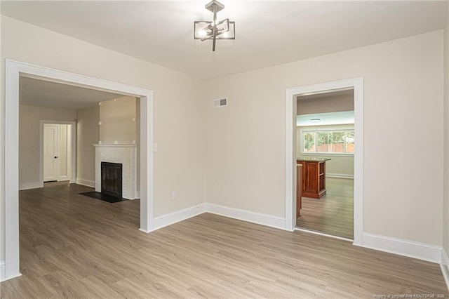 empty room featuring visible vents, a brick fireplace, light wood-style flooring, and baseboards