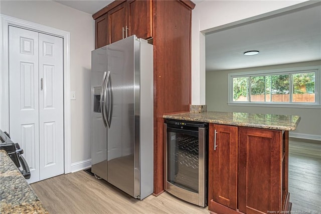 kitchen with stone counters, wine cooler, stainless steel fridge with ice dispenser, light wood-style floors, and baseboards