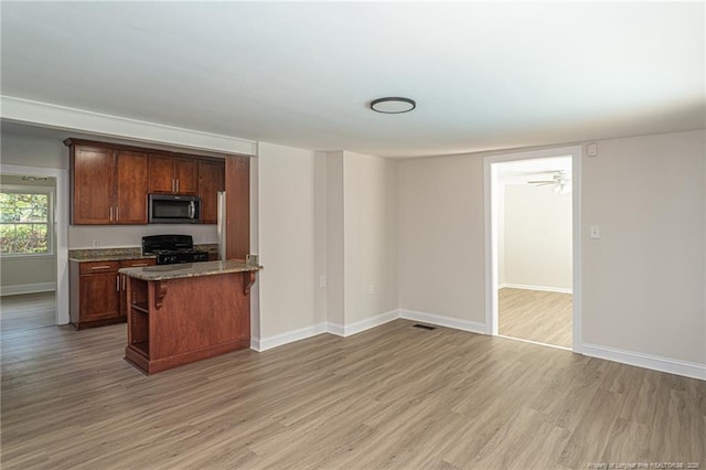 kitchen with stone counters, a breakfast bar, black gas stove, baseboards, and light wood-type flooring