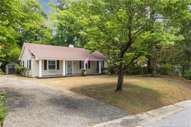 ranch-style home featuring covered porch, an outdoor structure, a front yard, a shed, and gravel driveway