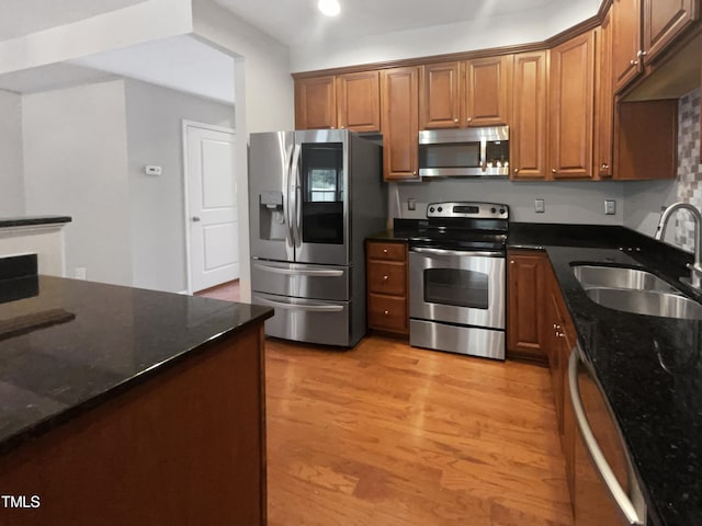 kitchen with dark stone counters, stainless steel appliances, light hardwood / wood-style floors, and sink