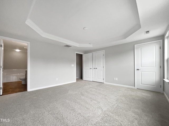 unfurnished bedroom with a closet, ensuite bath, a raised ceiling, and carpet floors