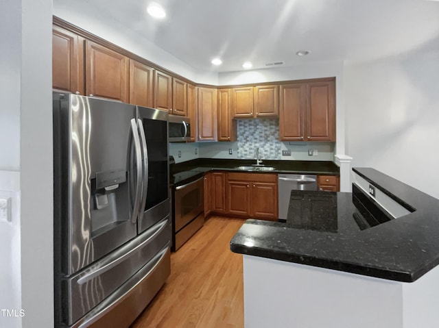 kitchen with stainless steel appliances, sink, kitchen peninsula, decorative backsplash, and light wood-type flooring