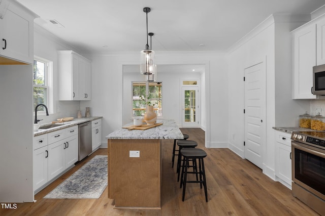 kitchen with light stone counters, decorative light fixtures, a center island, appliances with stainless steel finishes, and white cabinets