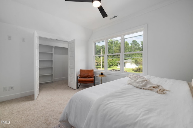 carpeted bedroom with ceiling fan, a walk in closet, and vaulted ceiling