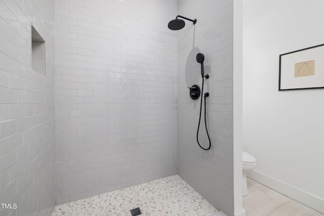 bathroom featuring hardwood / wood-style flooring, tiled shower, and toilet