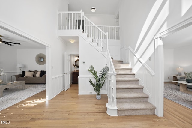 stairs with wood-type flooring, ornamental molding, ceiling fan, and a high ceiling