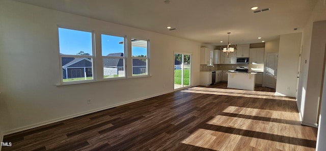 kitchen with a kitchen island, appliances with stainless steel finishes, pendant lighting, white cabinets, and dark wood-type flooring